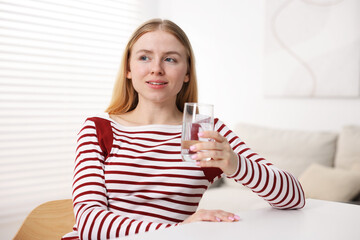 Young woman with glass of water at white table indoors