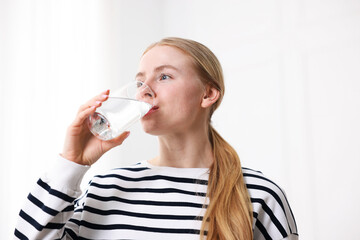 Young woman drinking water from glass on light background, low angle view