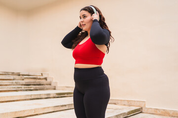 Curvy sportswoman wearing wireless headphones enjoying music during outdoor workout