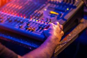 Close-up of a hand adjusting audio mixer controls at a live event. Concept of sound engineering, music production, and concert setup in vibrant stage lighting.
