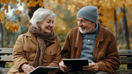 Happy senior couple using tablets on park bench in autumn, enjoying technology. - Powered by Adobe