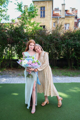 Teen graduate with sash and flowers celebrating with supportive friend, smiling together