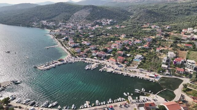 Drone hovers above the heart of Seget Vranjica revealing a compact village core with clustered rooftops, marina, streets and blue sea nearby on a sunny day