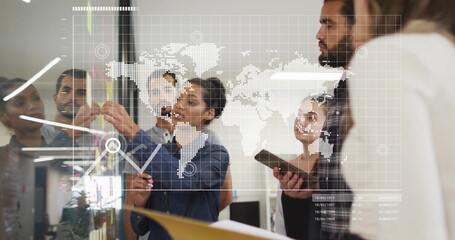 Collaborating five coworkers adding sticky notes, marking glass board with data overlay at office