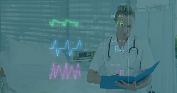 Holding clipboard nurse wearing scrubs and stethoscope reviewing vital waveforms in patient room