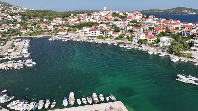 Aerial footage of the marina and riva in Seget Vranjica showing boats, piers, promenade and clear blue sea with local life and calm summer ambiance