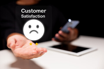 A person holds a holographic display showing a sad face and two-star rating for customer...