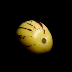 An artistic photograph featuring a pepino melon set against a dark background. The creamy yellow...