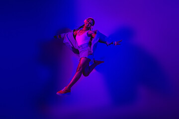 Young woman in neon lighting dancing stylishly in vibrant casual attire against colorful ultraviolet illuminated backdrop
