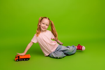 Young girl with toy truck on bright green background, wearing casual outfit, representing fun and...