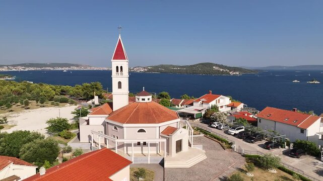 Aerial footage features a church on a hilltop overlooking Seget Vranjica, with surrounding sea views, terrain and village rooftops in the background