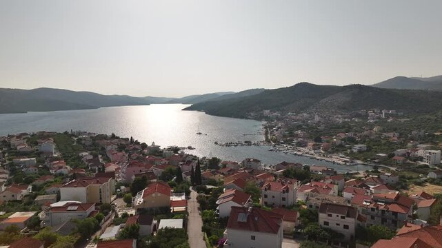 Drone shows the charming coastal town of Seget Vranjica located near Trogir with scenic sea, traditional rooftops and a calm harbor under soft afternoon light