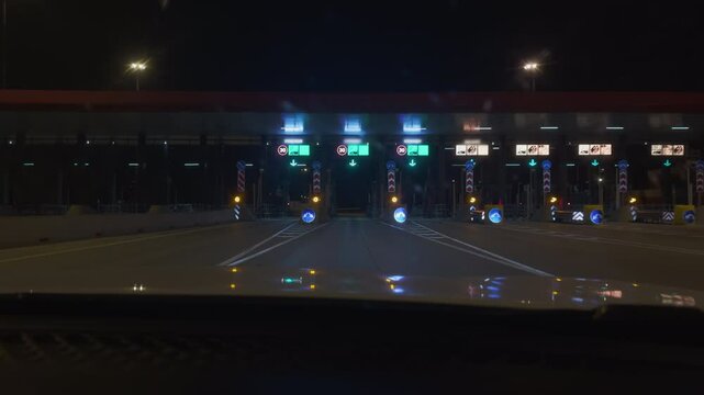 POV of a driver passing through a toll booth on a toll road at night. You drive a car through a contactless payment point on the road and a barrier opens in front of it. Modern motorways at night