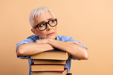 Thoughtful Senior Woman in Glasses Leaning on book Against Beige Background