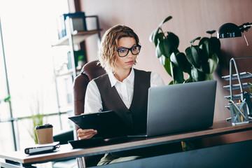Confident businesswoman in an elegant office, working at a laptop, reviewing documents in a...