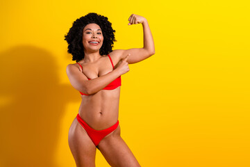 Charming young woman in red lingerie smiling and posing against a vibrant yellow background...