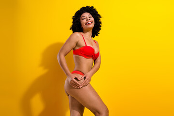 Confident young woman in red bikini posing against vibrant yellow background, celebrating body positivity and summer vibes