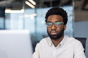 Naklejka premium A serious man with glasses looks directly at the camera in an office environment.