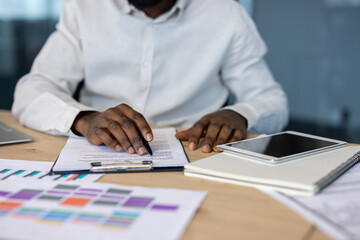 Close-up shot of a person's hands writing on a document at a desk. A tablet and notepad rest beside.