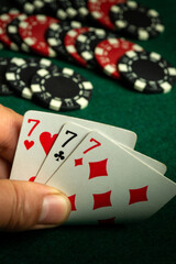 A close-up of a hand revealing three sevens in a poker game. The table is adorned with various red...