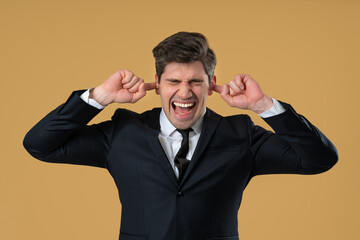 Businessman covering ears, showing irritation in beige studio. Stress, overload