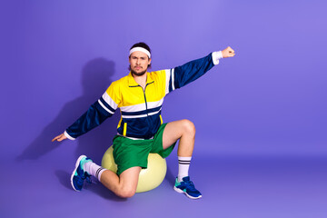 Sporty young man dressed in retro sportswear striking a confident pose against a purple background...