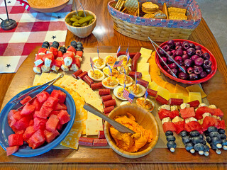 A vibrant charcuterie board is arranged with an assortment of cheeses, meats, and fruits, including watermelon and cherries, for a festive American patriotic party 