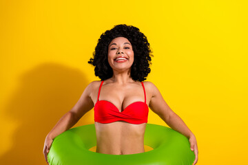 Playful woman in red bikini with green float on vibrant yellow background representing summer fun and relaxation