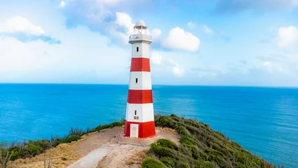 Red and white lighthouse is on a rocky cliff overlooking the ocean © dbrus