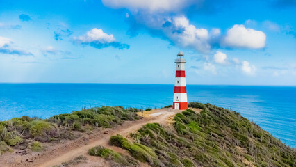 Red and white lighthouse is on a rocky cliff overlooking the ocean