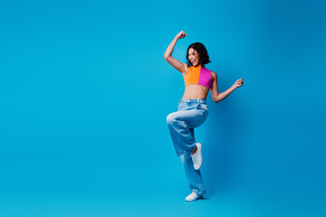 Cheerful Energetic young woman in vibrant outfit dancing joyfully against a vivid blue backdrop