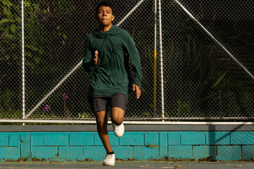 Latino teenager running fast in a straight line in a park in the morning, having a race while receiving the morning sun, healthy lifestyle