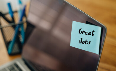 Good job message on sticky note, encouragement on laptop screen in office setting