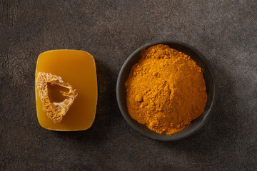Turmeric soap bar and powder turmeric root on dark brown background. Organic skincare product...