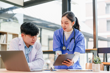 Medical professional and nurse discussing patient information with digital tablet and laptop in modern hospital office, teamwork and collaboration in healthcare setting