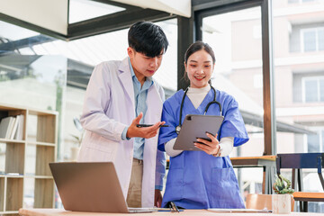 Two healthcare professionals, male doctor and female nurse, discuss patient information using digital tablet in modern medical office, appearing focused and collaborative