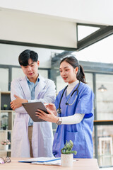 Two healthcare professionals, one male and one female, discussing patient information on digital tablet in modern medical office, teamwork and collaboration, natural light