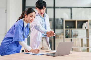 Two healthcare professionals, one male and one female, collaborate in modern medical office, discussing patient information on laptop with focused and positive expressions