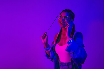 Young woman in neon lighting enjoying a phone call wearing denim jacket