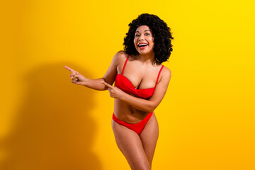 Cheerful woman in a red bikini posing against a yellow background, expressing joy and confidence,...