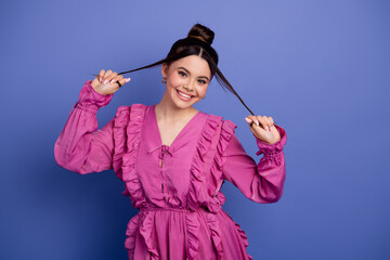 Young woman in a stylish pink dress posing playfully against a purple background, showcasing trendy...