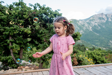 Cute funny little girl toddler child blowing soap bubbles in park summer outside