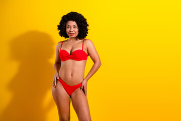 Confident woman posing in a red bikini on a bright yellow background showcasing beauty, fashion,...