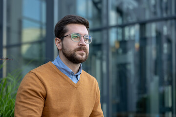 Close-up photo of a young male businessman standing outside, looking forward seriously and thoughtfully