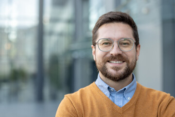 Close-up portrait of a young smiling and successful man standing outside and smiling at the camera