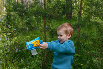 A smiling child holds a bubble gun in his hands while playing in nature. Soap bubbles.