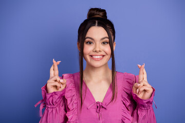 Portrait of a cheerful young woman crossing her fingers wishing luck, stylish in pink dress against...