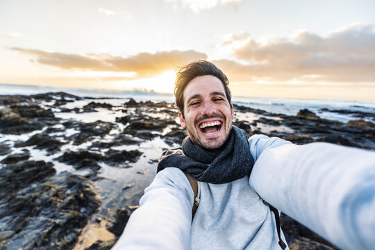 Handsome young man taking selfie pic with smart mobile phone outdoors - Traveler guy smiling at camera with sunset on background - Traveling life style and technology concept - Powered by Adobe