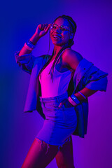 Vibrant young woman in trendy denim outfit with neon nightclub lighting and joyful expression capturing modern casual fashion