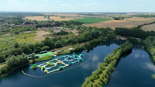 Aerial close up drone shot beautiful blue lakes and lush greenery with inflatable aqua water park play event near Little Paxton England UK